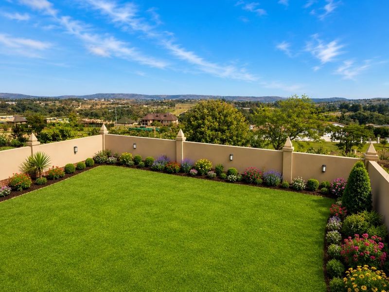 A well-maintained elevated garden area featuring a manicured lawn, landscaped flower beds, and a perimeter wall with integrated lighting, offering scenic landscape views.