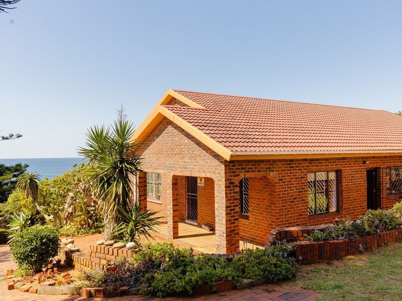 A well-maintained face brick house featuring a covered patio, tiled roof, and established garden with scenic ocean views.