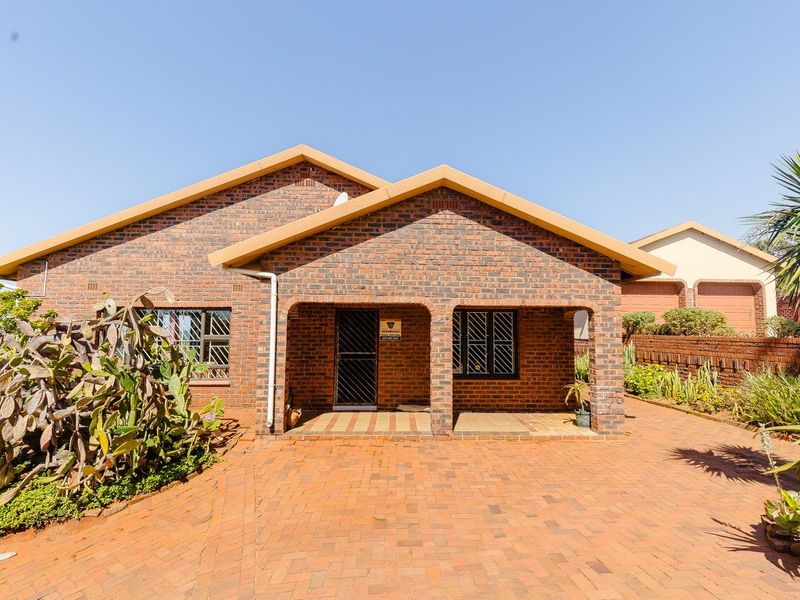A well-maintained face brick house featuring a paved driveway, covered front porch, and secure window bars, set within a neat garden.