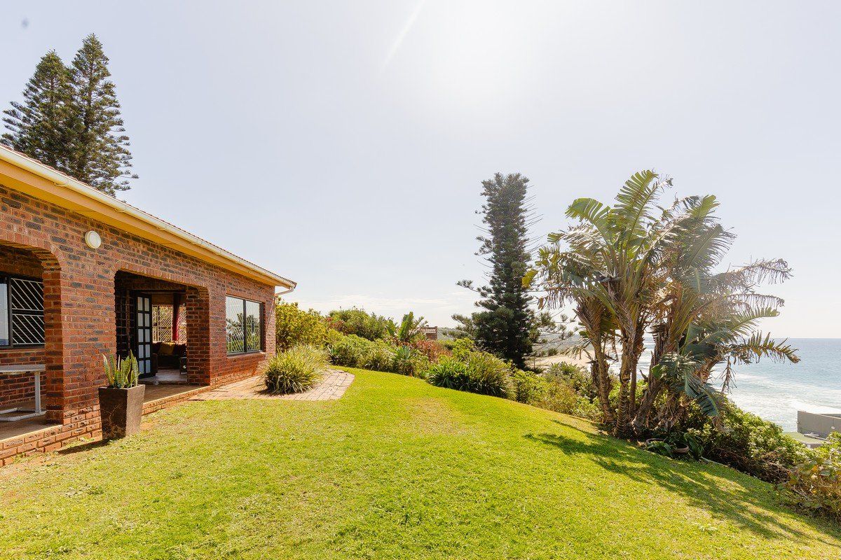 A rear view of a brick house featuring a covered patio, a well-maintained lawn, and scenic coastal views.