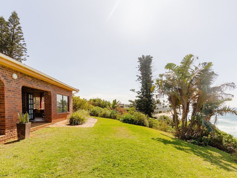 A rear view of a brick house featuring a covered patio, a well-maintained lawn, and scenic coastal views.