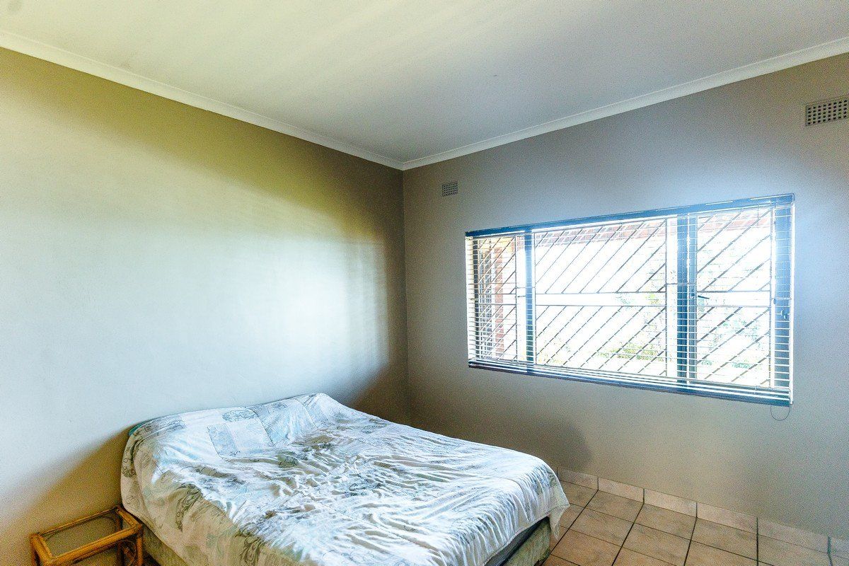 A functional bedroom featuring tiled flooring, security bars on the window, and neutral wall tones, offering a blank canvas for personalization.