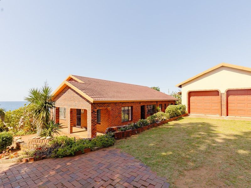 A well-maintained brick house featuring a tiled roof, double garage, and paved driveway, set within a landscaped garden with coastal views.