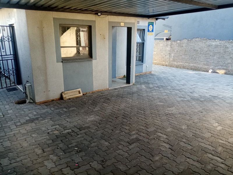 Front exterior view featuring a paved driveway, covered carport, and secure access with security gates and bars on windows.