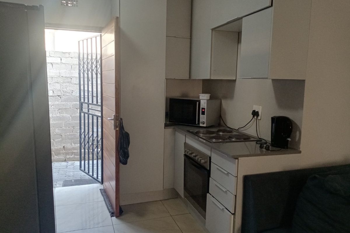 Compact kitchen featuring built-in cabinetry, an electric hob, and an oven, with direct access to an outdoor area through a security gate.