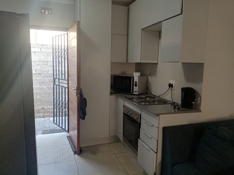 Compact kitchen featuring built-in cabinetry, an electric hob, and an oven, with direct access to an outdoor area through a security gate.
