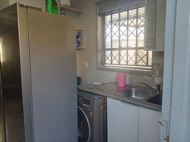 A functional laundry area featuring a stainless steel sink, built-in cabinetry, and security bars on the window, showing signs of wear on the wall finish.