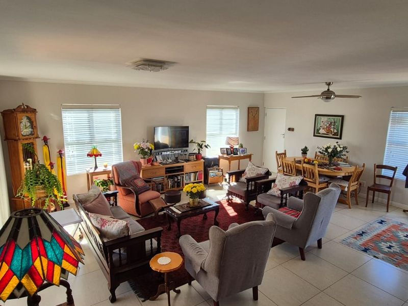 Spacious open-plan living and dining area featuring neutral tiled flooring, ceiling fan, and multiple windows with venetian blinds.
