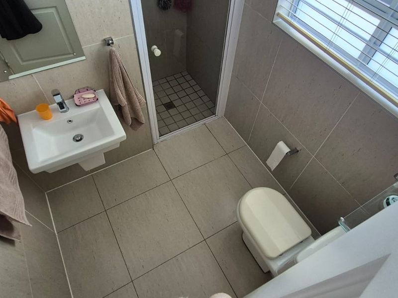A functional bathroom featuring a wall-mounted basin, a separate shower enclosure, and tiled finishes throughout.