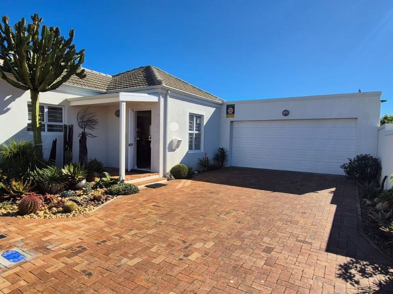 Front elevation of a well-maintained house featuring a brick-paved driveway, single garage, and a covered entrance with landscaped garden beds.