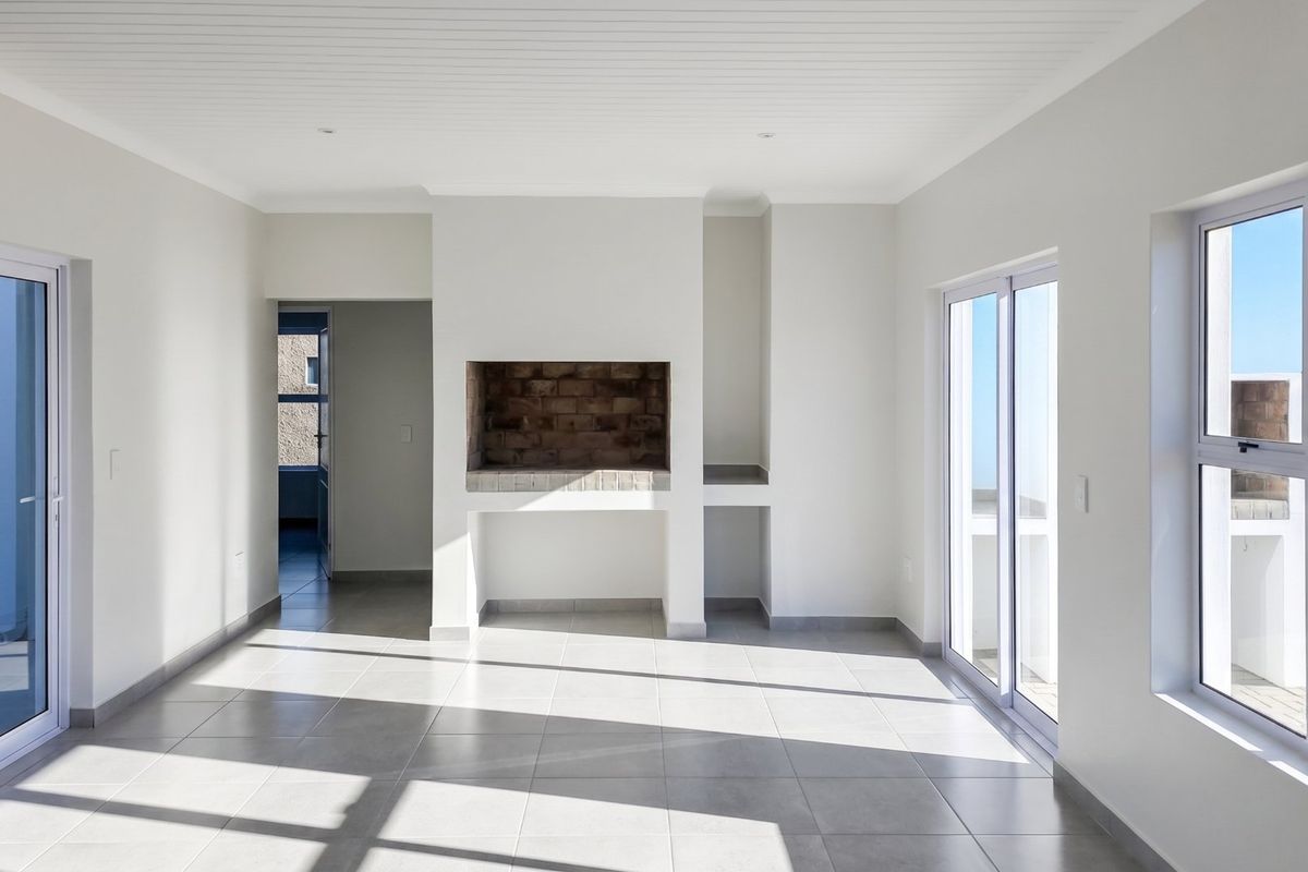 A bright, empty living room featuring tiled floors, a built-in fireplace, and large sliding glass doors providing ample natural light and outdoor access.