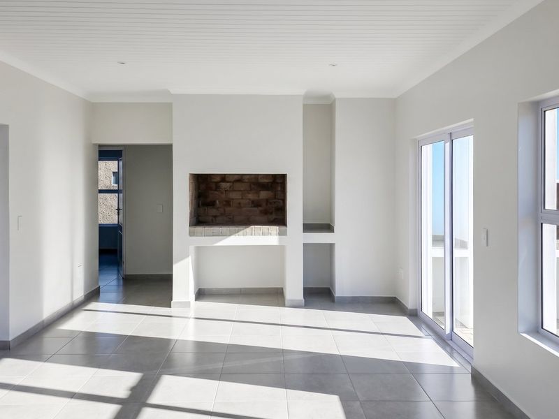 A bright, empty living room featuring tiled floors, a built-in fireplace, and large sliding glass doors providing ample natural light and outdoor access.