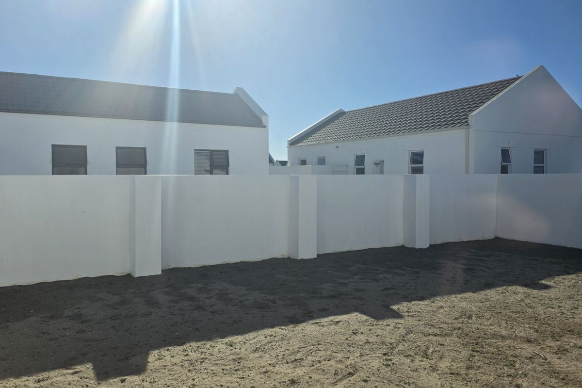 A rear view of the property featuring a clean white boundary wall and an unlandscaped garden area ready for development.