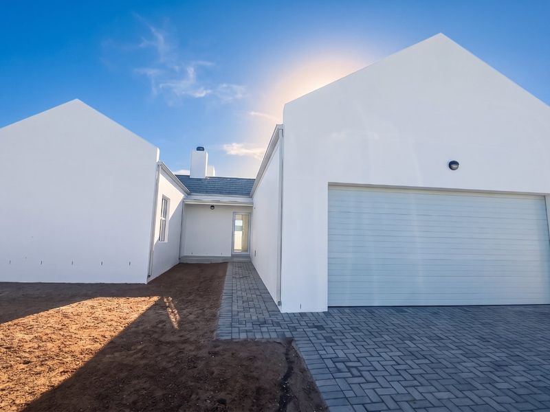Modern house exterior featuring a clean white facade, a double garage, and a paved driveway with surrounding unfinished garden space.