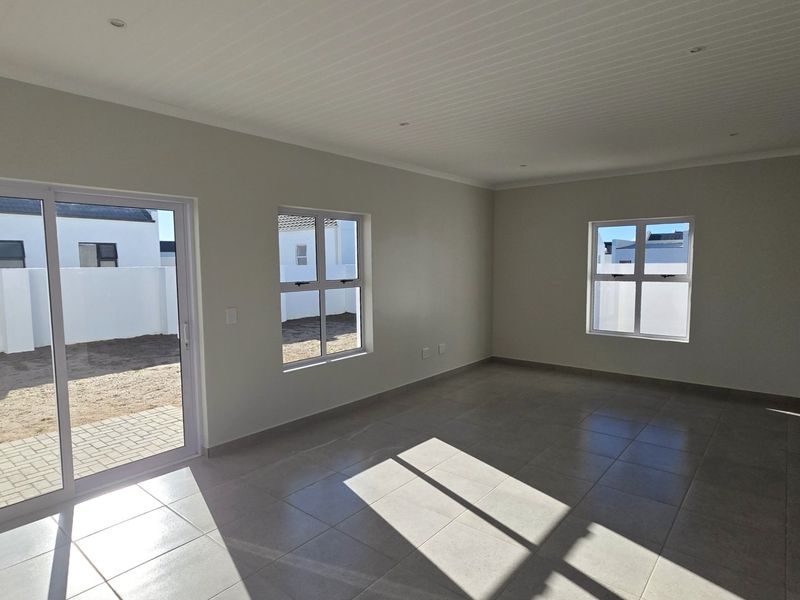 A bright, empty living room featuring neutral tiled flooring, recessed lighting, and a sliding glass door providing access to the rear exterior area.
