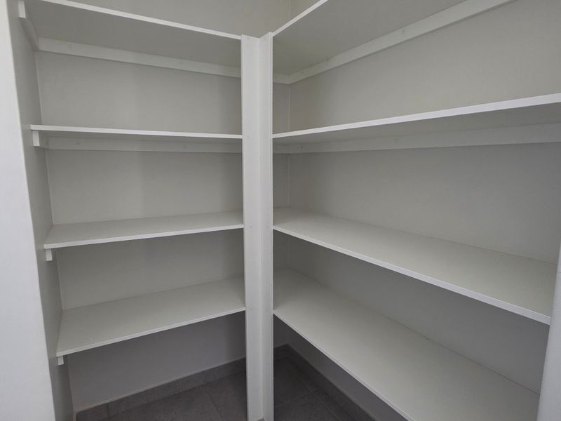 A clean, empty walk-in pantry or scullery featuring white built-in shelving units and tiled flooring.