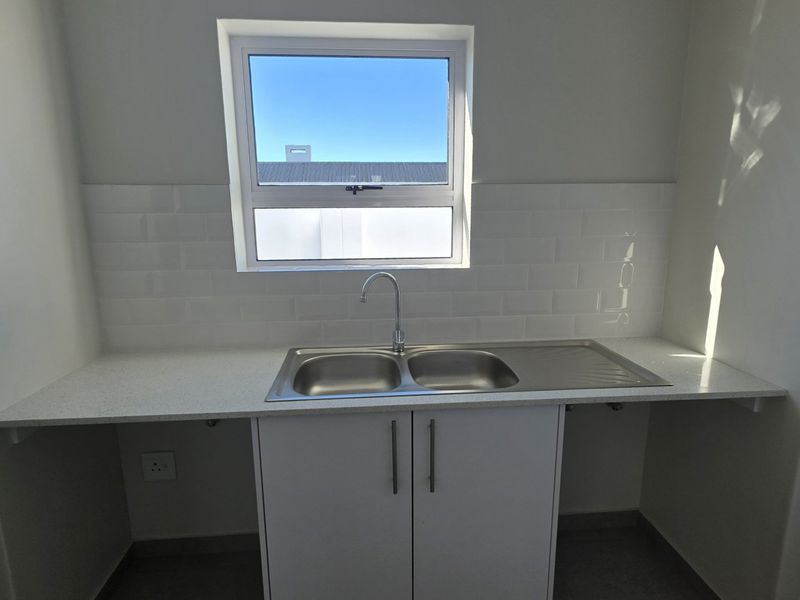 A clean and modern laundry area featuring a double bowl stainless steel sink, quartz countertops, and a stylish subway tile backsplash.