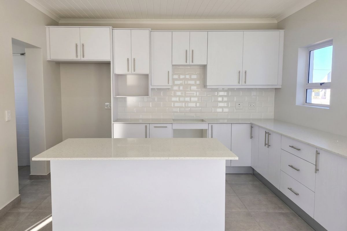 A modern, bright kitchen featuring white cabinetry, stone countertops, a subway tile backsplash, and a central island, finished with neutral floor tiles.