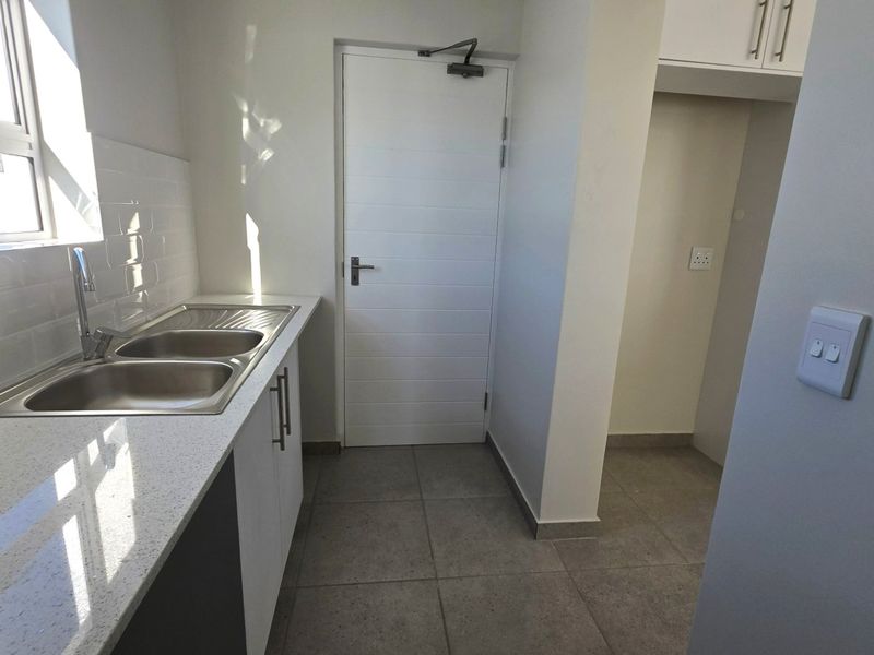 A clean and modern scullery featuring a double bowl stainless steel sink, stone countertops, subway tile splashback, and ample built-in cabinetry.