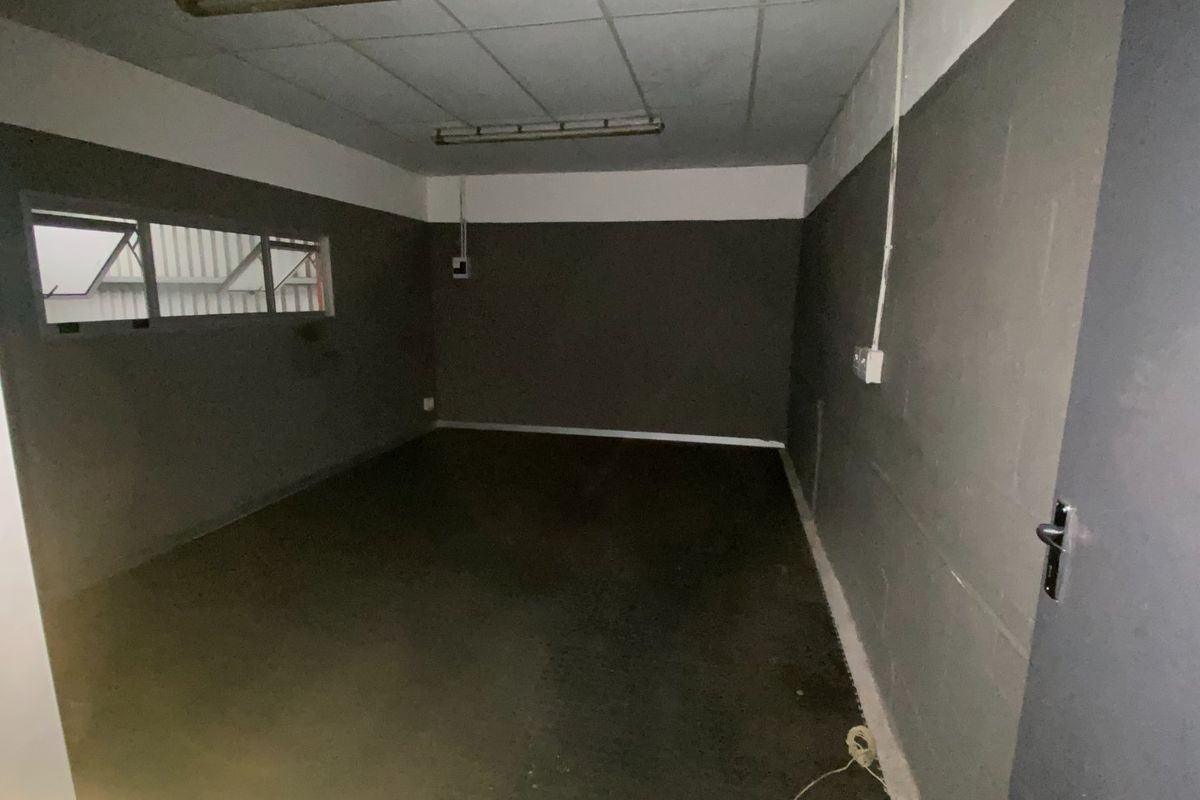An empty industrial utility space featuring concrete flooring, exposed electrical conduit, and fluorescent strip lighting, suitable for storage or workshop use.