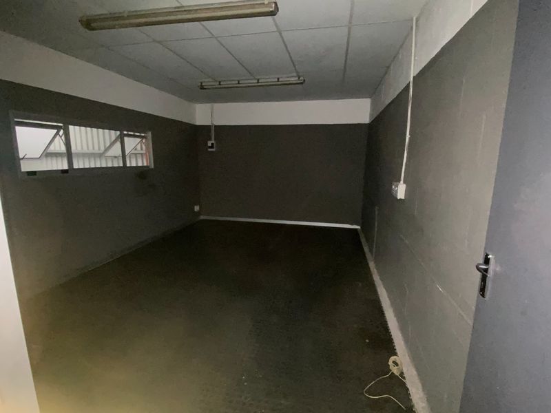 An empty industrial utility space featuring concrete flooring, exposed electrical conduit, and fluorescent strip lighting, suitable for storage or workshop use.