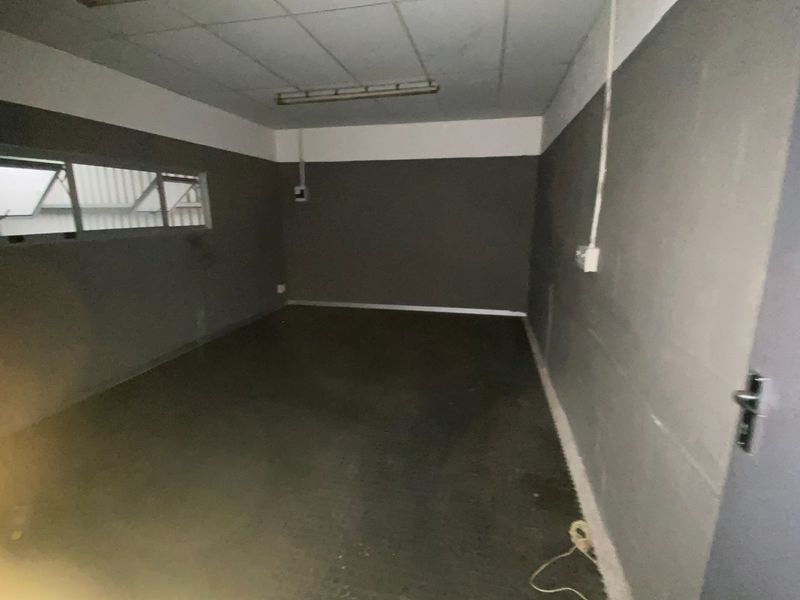 An empty, functional utility space featuring a suspended ceiling, fluorescent lighting, and horizontal sliding windows, suitable for storage or workshop use.