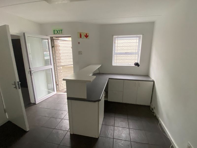 A functional industrial reception area featuring a built-in service counter, tiled flooring, and direct access to the exterior via a security gate.