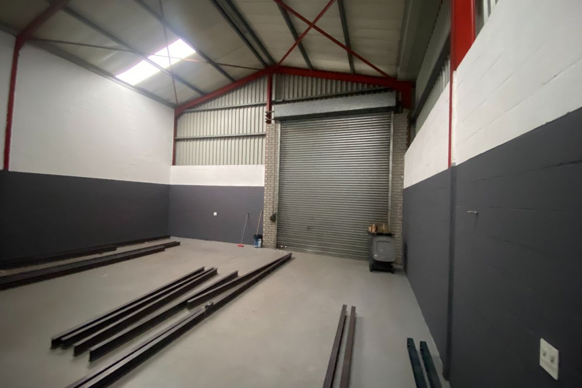 Spacious industrial warehouse unit featuring a high-clearance steel portal frame, concrete flooring, and a large roller shutter door for vehicle or equipment access.