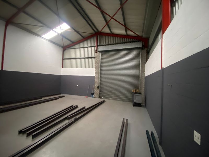 Spacious industrial warehouse unit featuring a high-clearance steel portal frame, concrete flooring, and a large roller shutter door for vehicle or equipment access.