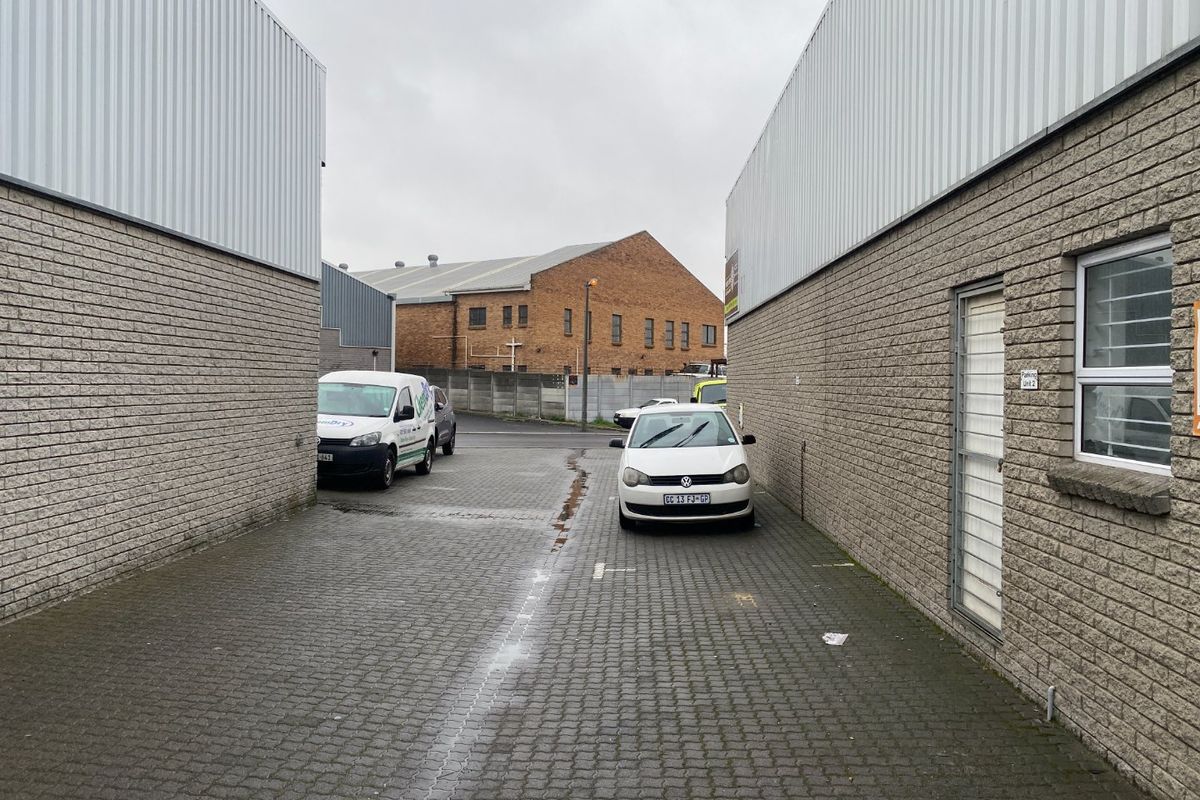 Exterior view of an industrial property featuring concrete block walls, corrugated metal cladding, and a paved driveway area.