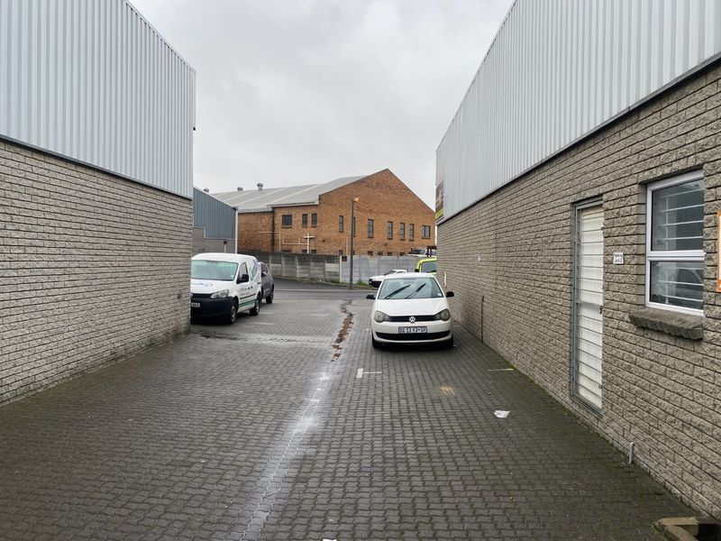 Exterior view of an industrial property featuring concrete block walls, corrugated metal cladding, and a paved driveway area.