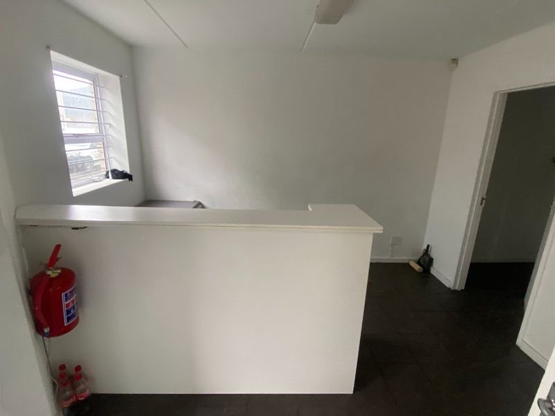 An empty office space featuring a built-in service counter, tiled flooring, and a louvered window, suitable for a reception or administrative area.