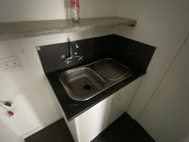 A compact scullery or utility area featuring a stainless steel sink, tiled splashback, built-in base cabinetry, and a wall-mounted shelf.
