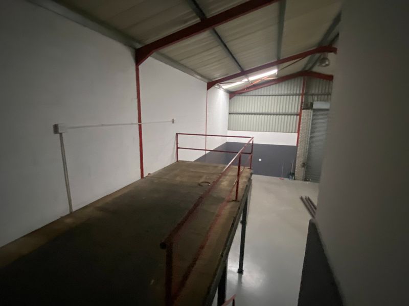 Industrial utility space featuring a mezzanine level with metal safety railings, exposed steel structural beams, and a roller shutter door.