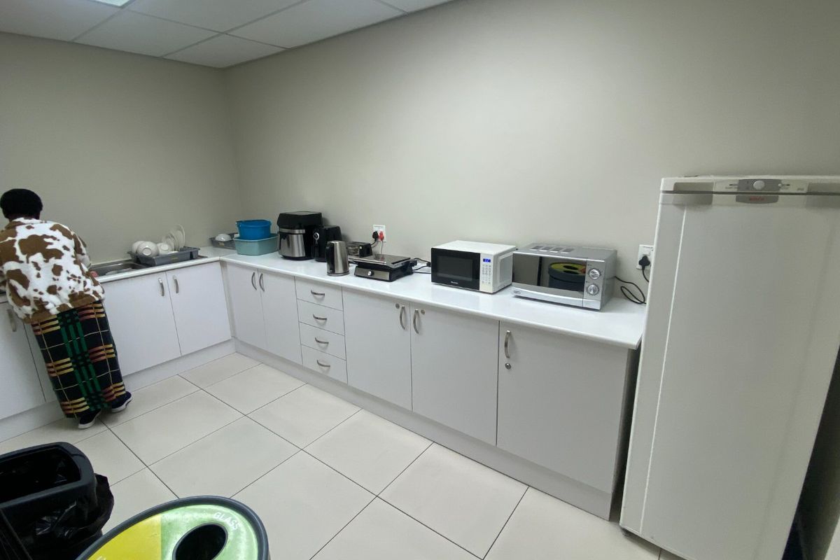A functional commercial kitchenette featuring white built-in cabinetry, laminate countertops, a sink, and tiled flooring with a drop ceiling.