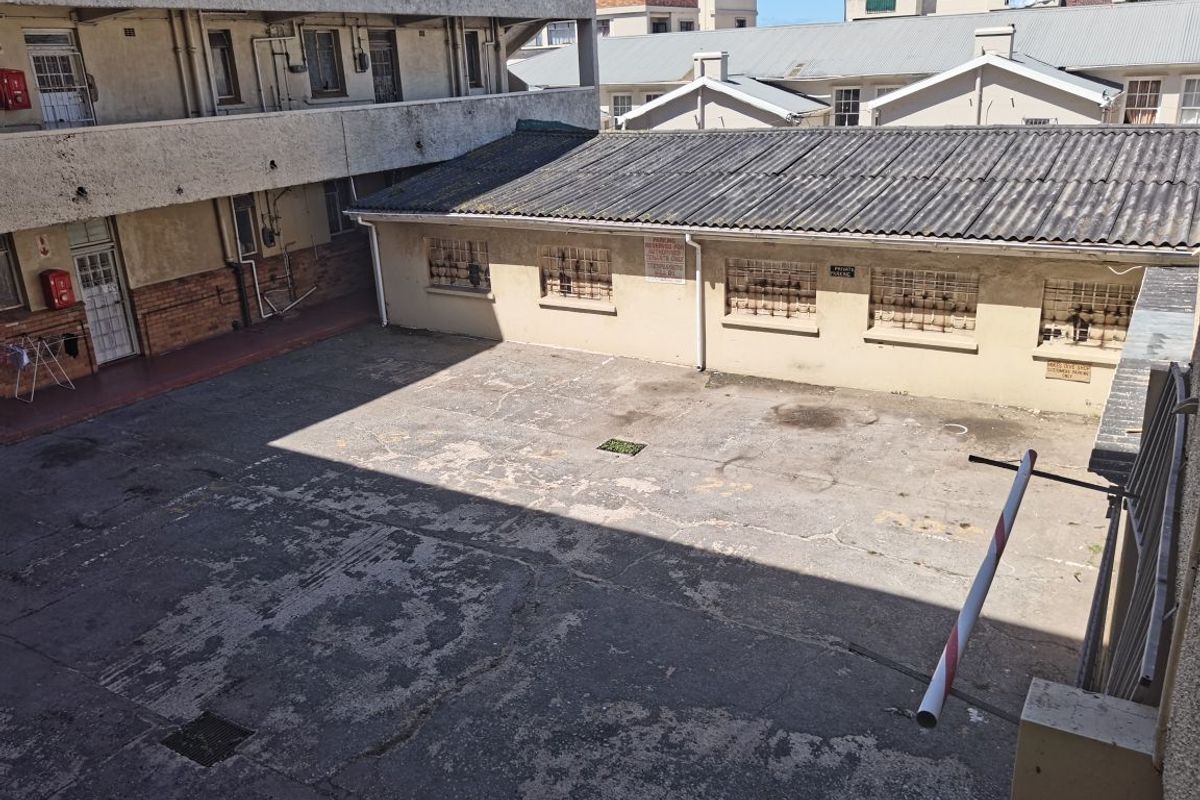 An elevated view of a paved courtyard area featuring a concrete surface, security-barred windows, and a parking boom gate.