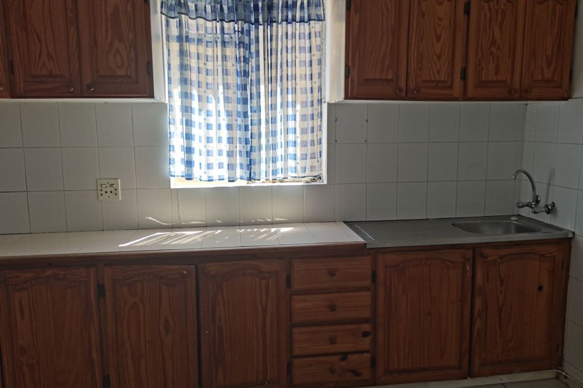 A dated kitchen featuring wooden cabinetry, tiled countertops, and a stainless steel sink, offering a blank canvas for potential renovation and modernization.