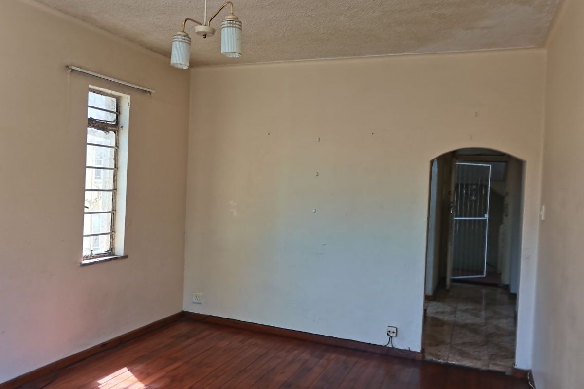 An empty living room featuring original hardwood flooring, an arched doorway, and a classic steel-framed window, offering a blank canvas for renovation.