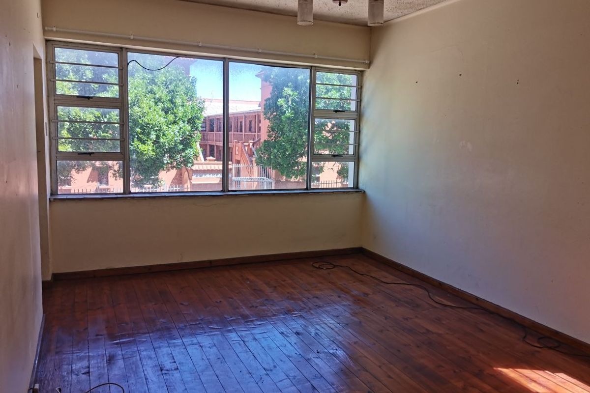 An empty bedroom featuring original timber flooring, large steel-framed windows, and a simple ceiling light fixture, offering a blank canvas for renovation.