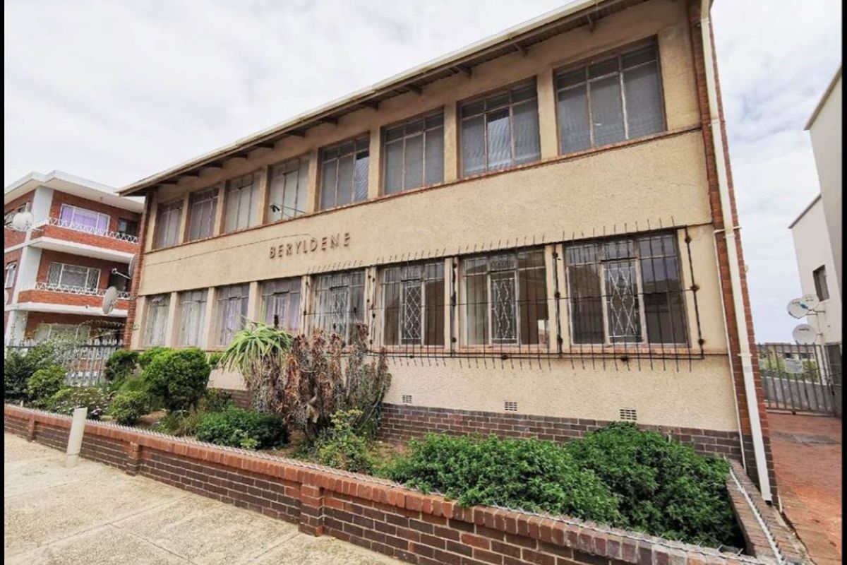 Exterior view of the Beryldene apartment building featuring a brick boundary wall, security bars on windows, and a stucco facade.