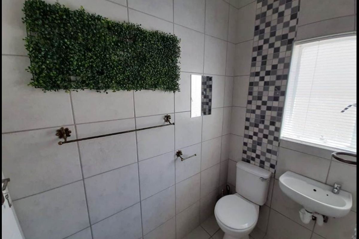 A compact bathroom featuring tiled walls with a decorative mosaic accent, a wall-mounted basin, and a standard toilet.