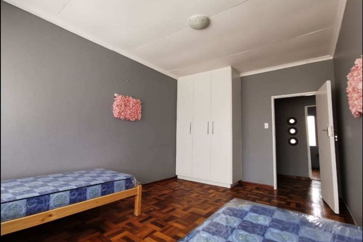 A bedroom featuring dark parquet flooring, grey painted walls, and a white built-in wardrobe.