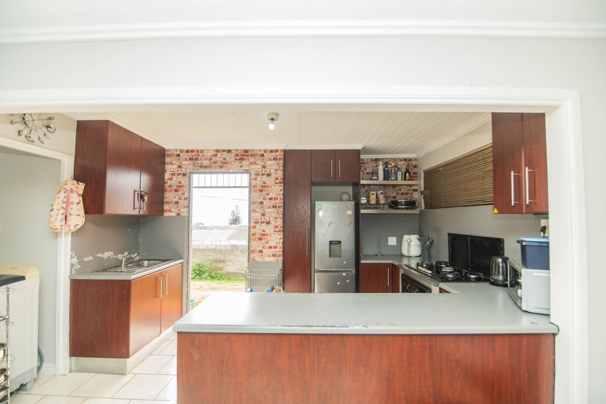 A dated kitchen featuring dark wood cabinetry, a gas hob, and an exposed brick accent wall with direct access to the rear exterior.