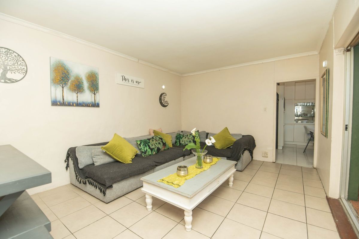 A functional living room featuring neutral tiled flooring and coving, with an open transition leading into the adjacent kitchen area.