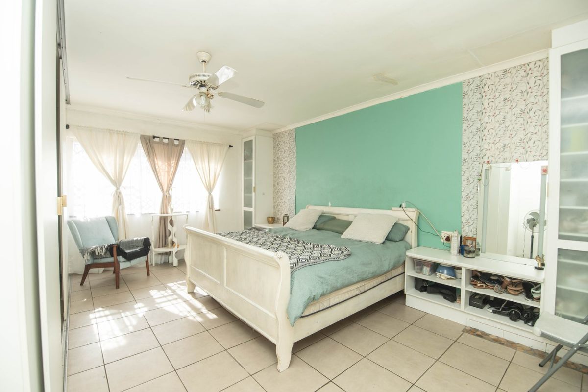 A bedroom featuring tiled flooring, a ceiling fan, and built-in storage, showing signs of wear including ceiling staining and wall paint deterioration.