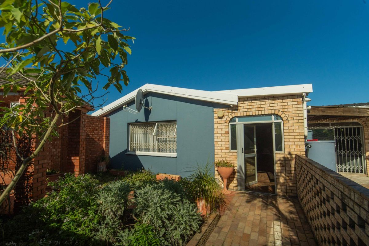 Rear view of the property featuring a paved courtyard, brick boundary walls, and a secure entrance with security gate and bars.