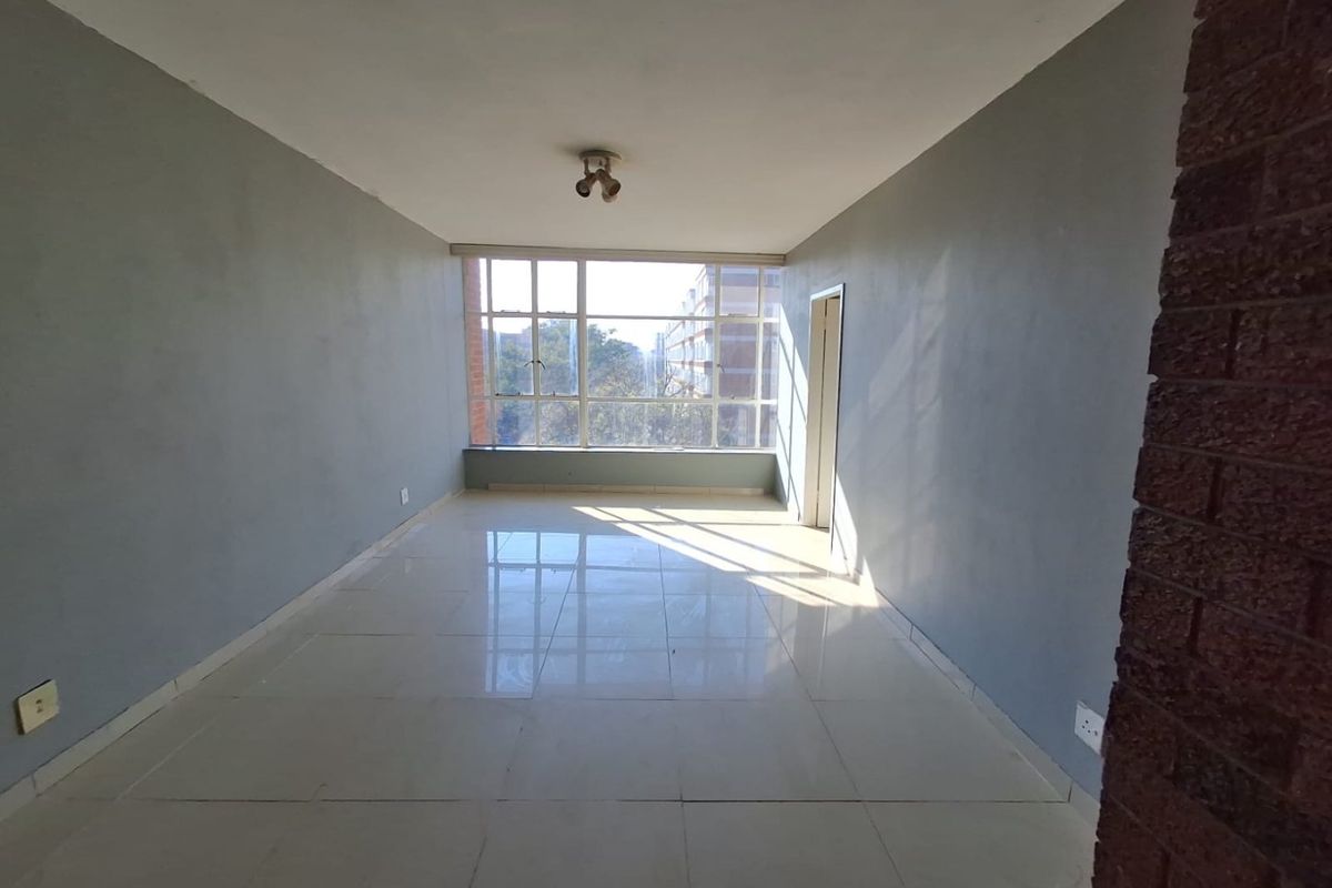 A bright, empty living room featuring large windows, tiled flooring, and an exposed brick accent pillar, offering a clean canvas for interior design.