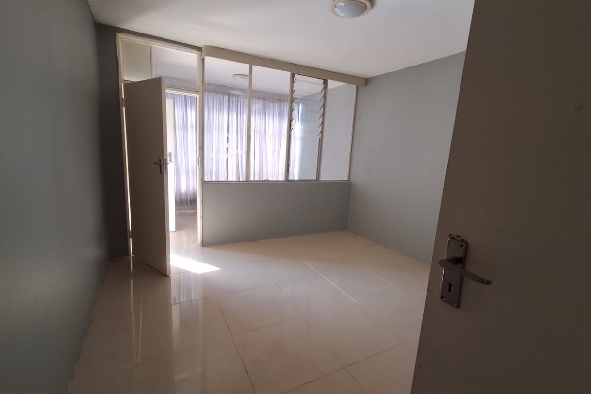 An empty bedroom featuring tiled flooring, a glass partition wall, and neutral grey walls, offering a clean and versatile space.