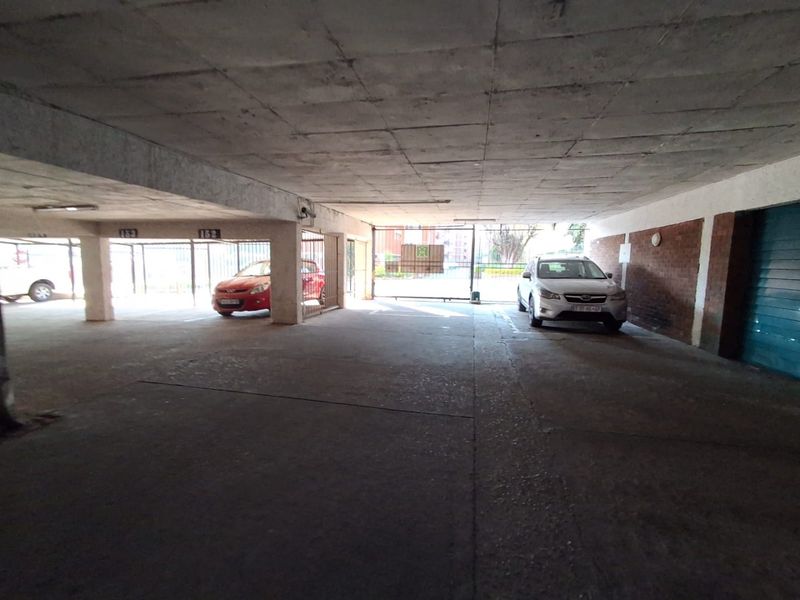 A covered parking garage area featuring concrete flooring, exposed concrete ceiling, and secure gated access.