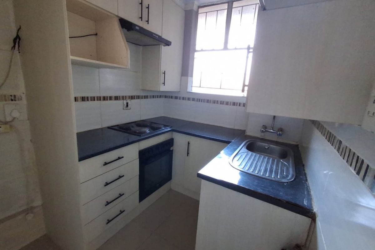 Compact kitchen featuring built-in cabinetry, electric hob, oven, extractor fan, and a stainless steel sink with tiled backsplash.